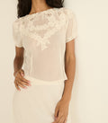 Woman wearing a sheer white lace top against a plain background