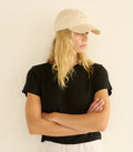 Woman wearing a black t-shirt and beige cap against a plain background