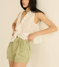 Woman wearing a white sleeveless top and green shorts on a plain background