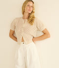Woman wearing a beige knitted cardigan over a white top and pants on a plain background