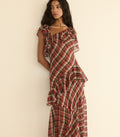 A woman wearing a red and cream plaid ruffled dress, posing against a plain beige wall.