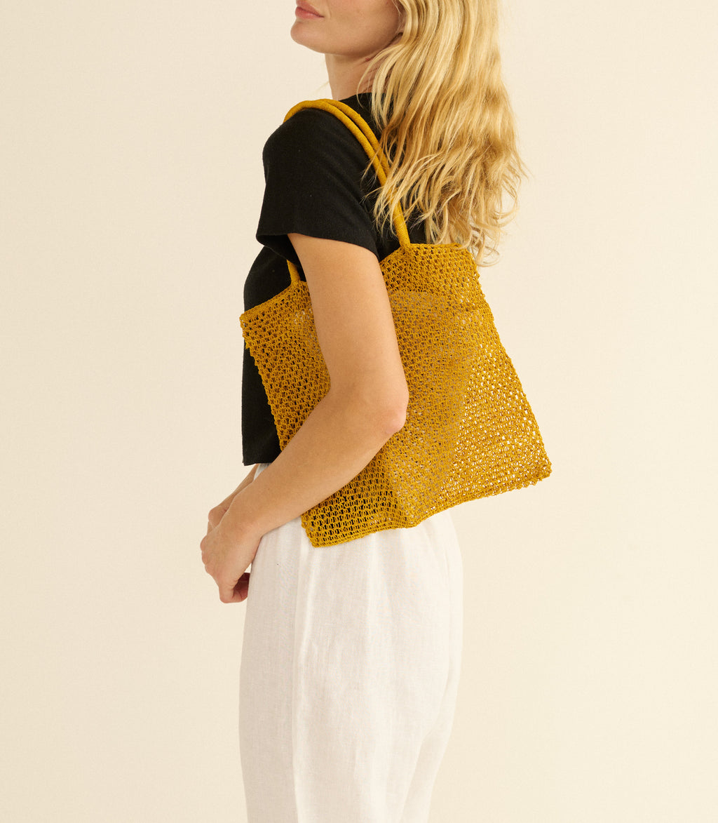 Woman holding a yellow knitted tote bag against a beige background