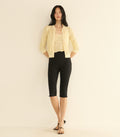 Woman wearing a light yellow cardigan and black capri pants on a beige background