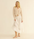 Woman wearing a beige pointelle cardigan and white skirt on a beige background